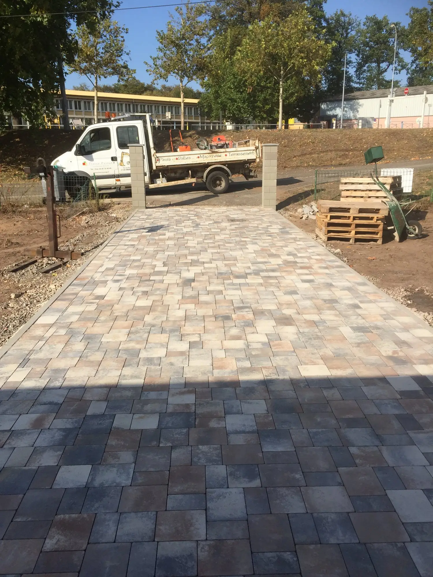 Chantier de pose de pavés en cours, avec engin de terrassement et fondation compactée