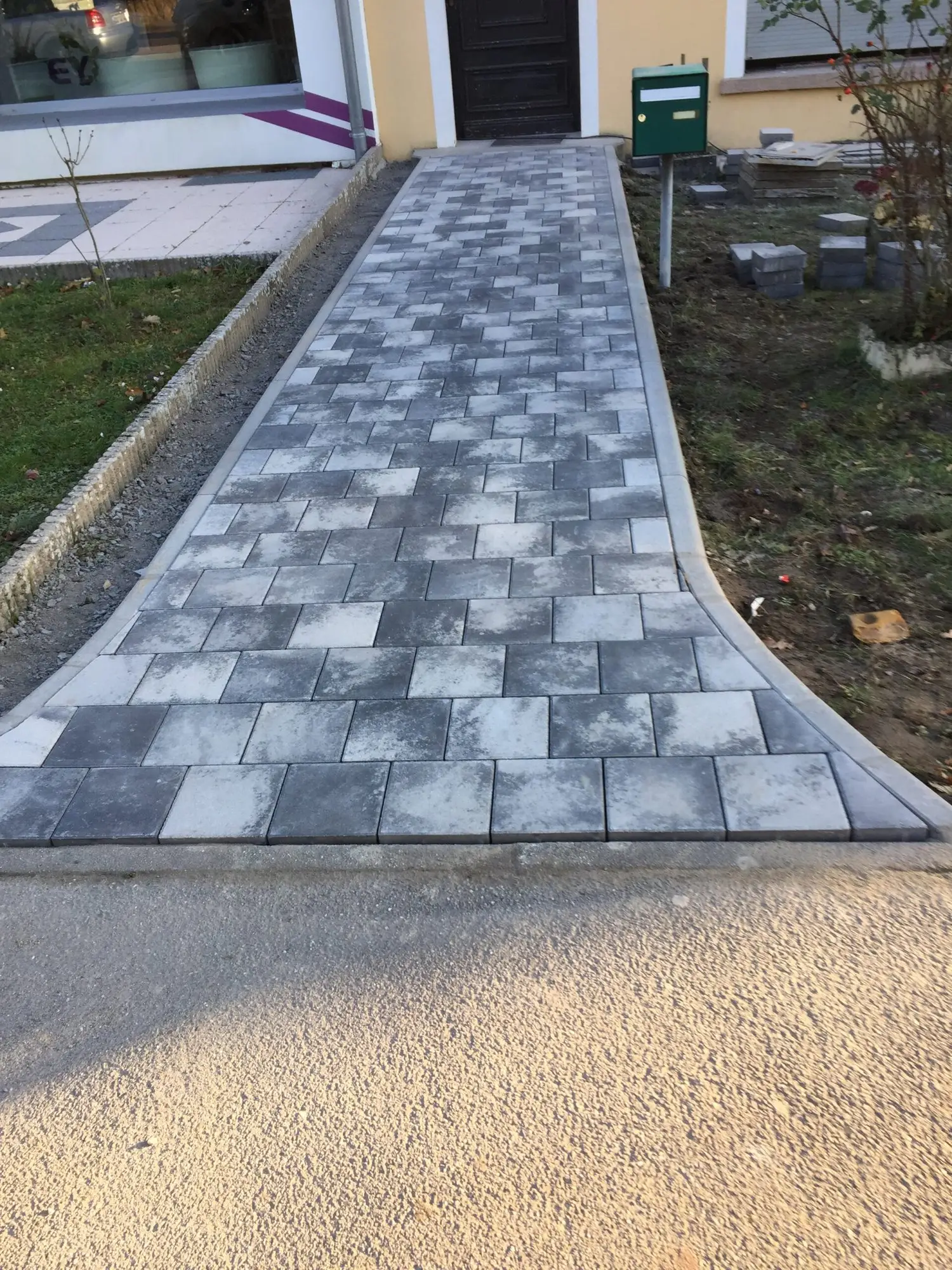Allée en pavés gris posée en calepinage régulier, cheminant à travers une pelouse