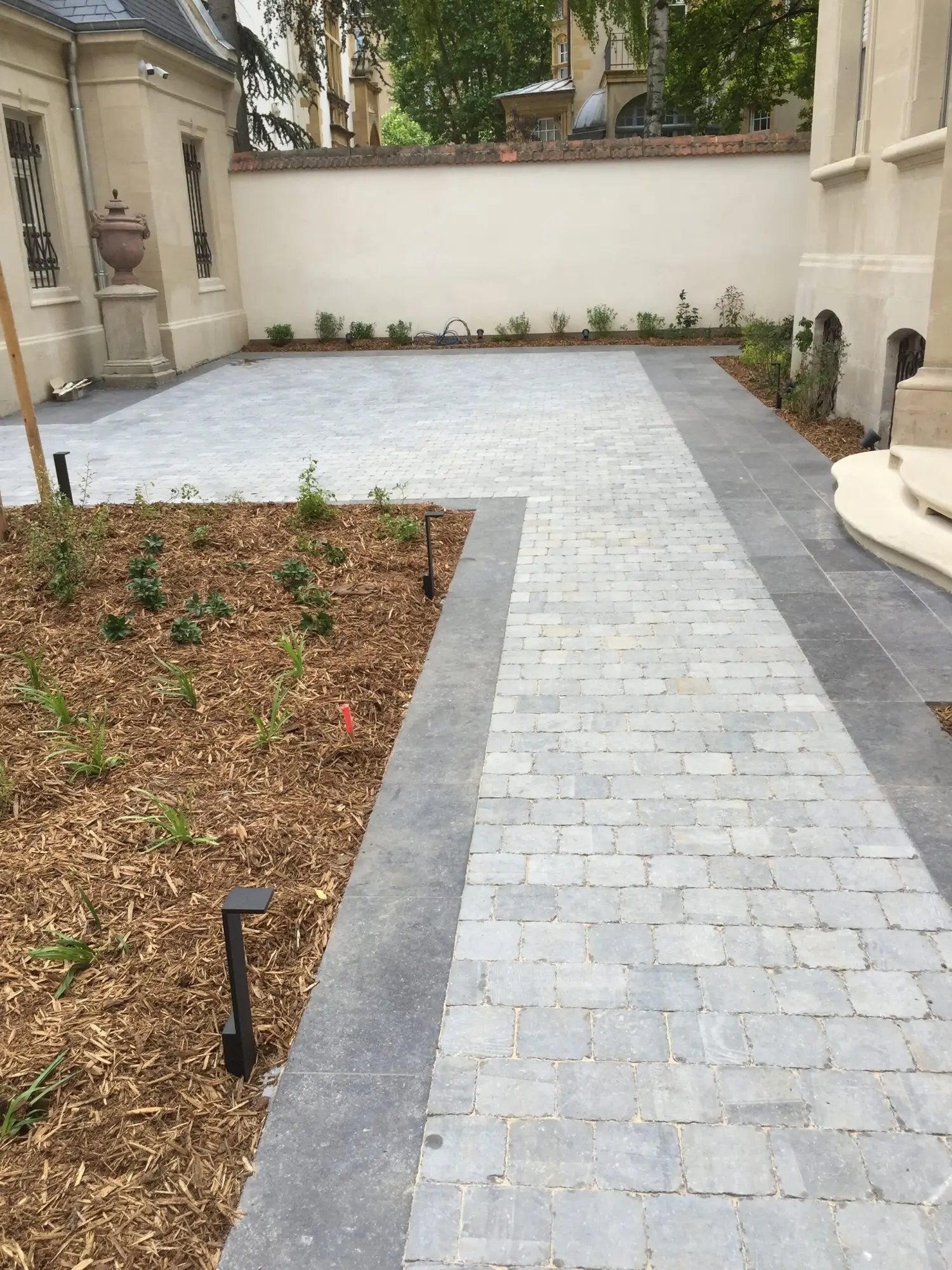 Cour pavée claire avec bordures et massifs plantés le long d’une maison