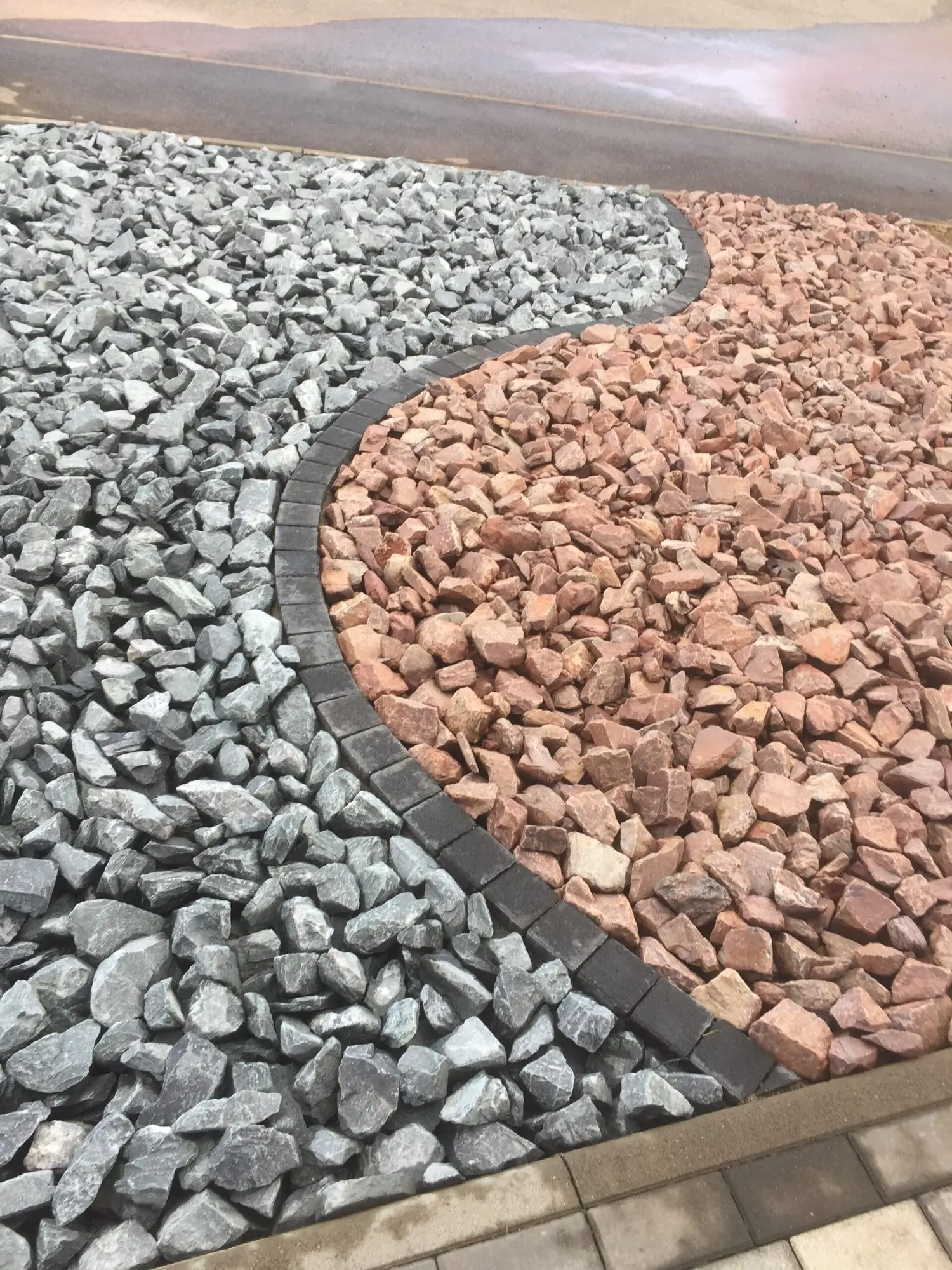 Massif décoratif en graviers gris et roses séparés par une bordure courbe en pavés